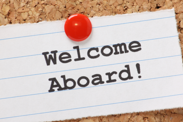 Pin holding up a note that says Welcome Aboard on cork bulletin board