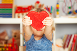 Child holding a toy heart in front of their face.