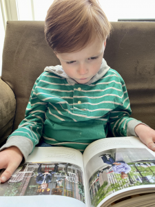 A young boy with a CACNA1C variation that causes many symptoms, including LGS, reads a large book on this lap.