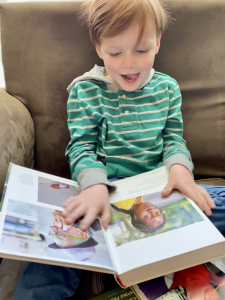 A young boy smiles as he looks at a book with people's faces.